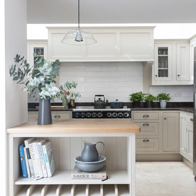 Beach style travertine floor kitchen photo in London with shaker cabinets, white cabinets, white backsplash, subway tile backsplash and a peninsula