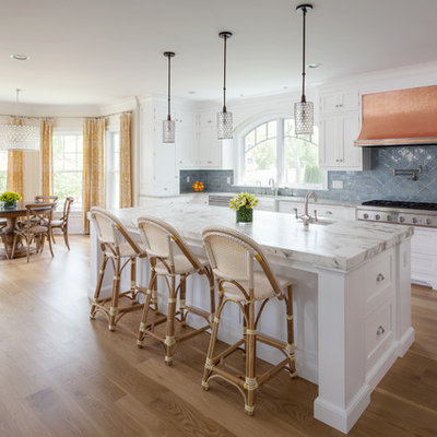 Example of a beach style galley medium tone wood floor eat-in kitchen design in Baltimore with a farmhouse sink, white cabinets, marble countertops, blue backsplash, ceramic backsplash, stainless steel appliances, an island and shaker cabinets