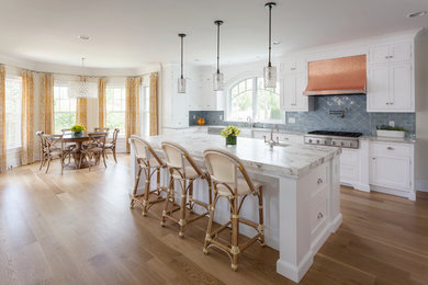 Example of a beach style galley medium tone wood floor eat-in kitchen design in Baltimore with a farmhouse sink, white cabinets, marble countertops, blue backsplash, ceramic backsplash, stainless steel appliances, an island and shaker cabinets