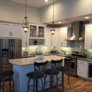 Mid-sized beach style l-shaped open plan kitchen in New York with recessed-panel cabinets, white cabinets, laminate benchtops, grey splashback, with island, an undermount sink, matchstick tile splashback, stainless steel appliances and medium hardwood floors.
