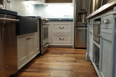 Eat-in kitchen - large coastal u-shaped light wood floor eat-in kitchen idea in New York with a farmhouse sink, blue cabinets, soapstone countertops, gray backsplash, stainless steel appliances, an island and recessed-panel cabinets