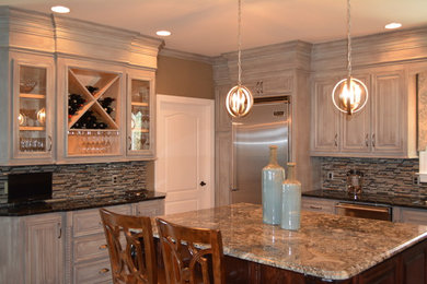 Mid-sized transitional l-shaped enclosed kitchen photo in Other with raised-panel cabinets, distressed cabinets, granite countertops, beige backsplash, matchstick tile backsplash, stainless steel appliances and an island