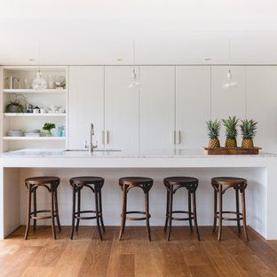 This is an example of a large contemporary l-shaped kitchen in Sydney with an undermount sink, flat-panel cabinets, white cabinets, mirror splashback, panelled appliances, with island, brown floor and white benchtop.