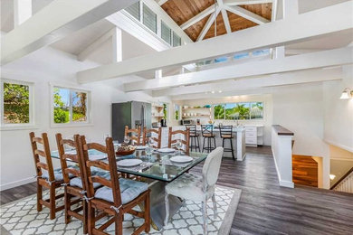Large nautical l-shaped open plan kitchen in Hawaii with a belfast sink, shaker cabinets, white cabinets, quartz worktops, stainless steel appliances, dark hardwood flooring, an island, brown floors and white worktops.