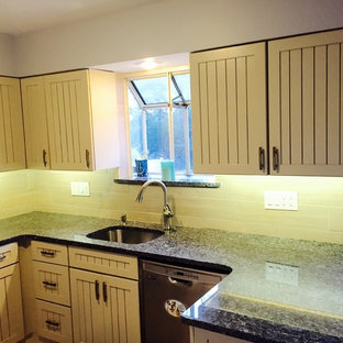 Photo of a mid-sized beach style l-shaped eat-in kitchen in San Diego with an undermount sink, louvered cabinets, beige cabinets, granite benchtops, beige splashback, porcelain splashback, white appliances, laminate floors and a peninsula.