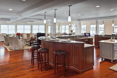 Example of a large transitional u-shaped dark wood floor eat-in kitchen design in Other with a farmhouse sink, raised-panel cabinets, dark wood cabinets, quartz countertops, beige backsplash, stone tile backsplash, stainless steel appliances and two islands
