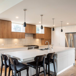Large contemporary l-shaped open plan kitchen in Melbourne with an undermount sink, flat-panel cabinets, white cabinets, concrete benchtops, beige splashback, ceramic splashback, stainless steel appliances, medium hardwood floors, with island, grey benchtop and brown floor.