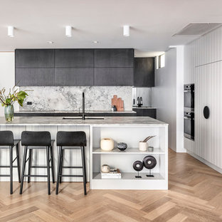 Photo of a beach style l-shaped kitchen in Sydney with black cabinets, marble benchtops, with island, an undermount sink, white splashback, black appliances, light hardwood floors, beige floor and white benchtop.