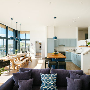 Beach style l-shaped open plan kitchen in Cornwall with a submerged sink, shaker cabinets, blue cabinets, white splashback, light hardwood flooring, an island, beige floors and white worktops.