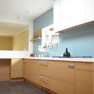 Imagen de cocina minimalista con armarios con paneles lisos, puertas de armario de madera clara, salpicadero azul y salpicadero de vidrio templado