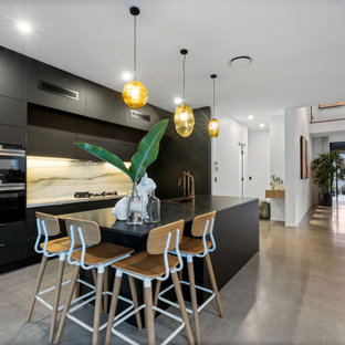 Inspiration for a contemporary galley kitchen in Sunshine Coast with an undermount sink, flat-panel cabinets, black cabinets, white splashback, stone slab splashback, black appliances, concrete floors, with island, grey floor and white benchtop.