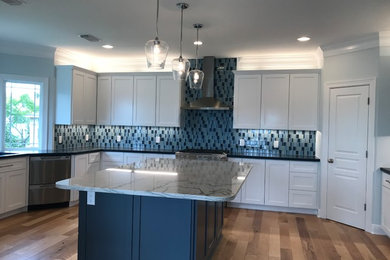 Eat-in kitchen - large coastal l-shaped light wood floor and brown floor eat-in kitchen idea in Houston with an undermount sink, shaker cabinets, white cabinets, quartzite countertops, blue backsplash, glass sheet backsplash, stainless steel appliances and an island
