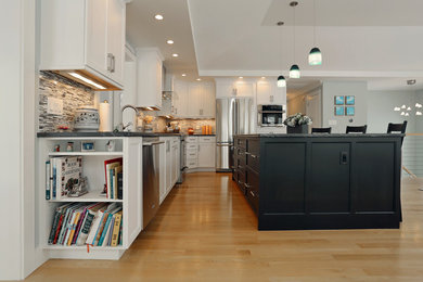 Open concept kitchen - mid-sized transitional l-shaped light wood floor open concept kitchen idea in Boston with white cabinets, granite countertops, an island, an undermount sink, shaker cabinets, gray backsplash, matchstick tile backsplash and stainless steel appliances
