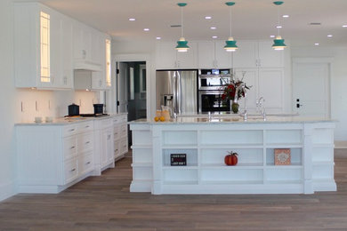 Example of a large beach style single-wall laminate floor open concept kitchen design in Miami with white cabinets, quartz countertops, white backsplash, stainless steel appliances, two islands and shaker cabinets