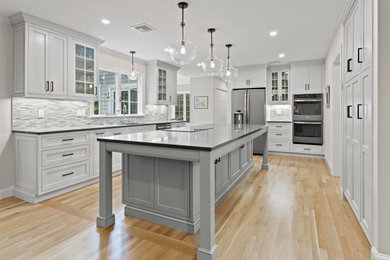 Inspiration for a transitional u-shaped light wood floor and beige floor kitchen remodel in Boston with an undermount sink, shaker cabinets, white cabinets, gray backsplash, mosaic tile backsplash, stainless steel appliances, an island and gray countertops