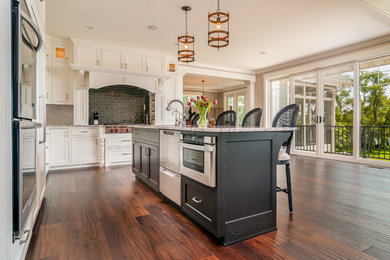 Example of a large transitional l-shaped dark wood floor open concept kitchen design in Milwaukee with an undermount sink, shaker cabinets, white cabinets, granite countertops, green backsplash, subway tile backsplash, stainless steel appliances and an island