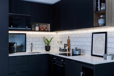 This is an example of a contemporary l-shaped open plan kitchen in London with flat-panel cabinets, black cabinets, engineered stone countertops, black appliances, no island and white worktops.