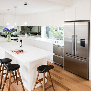 Inspiration for a mid-sized contemporary l-shaped eat-in kitchen in Melbourne with an integrated sink, flat-panel cabinets, white cabinets, solid surface benchtops, mirror splashback, stainless steel appliances, medium hardwood floors, with island, metallic splashback and white benchtop.