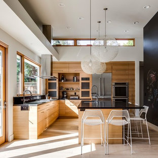 Photo of a large contemporary l-shaped eat-in kitchen in San Francisco with an undermount sink, flat-panel cabinets, medium wood cabinets, black splashback, stainless steel appliances, light hardwood floors, with island, beige floor and black benchtop.