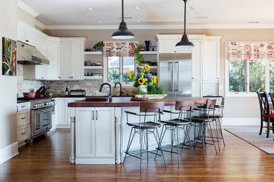 Inspiration for a large cottage l-shaped medium tone wood floor open concept kitchen remodel in Charlotte with shaker cabinets, white cabinets, stainless steel appliances, an undermount sink, wood countertops, multicolored backsplash, stone tile backsplash and an island
