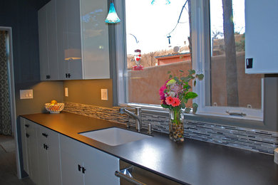 Enclosed kitchen - small contemporary galley ceramic tile enclosed kitchen idea in Albuquerque with an undermount sink, glass-front cabinets, white cabinets, solid surface countertops, multicolored backsplash, glass sheet backsplash, stainless steel appliances and no island