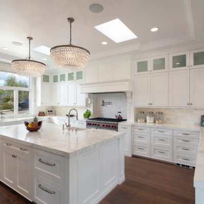 Huge transitional u-shaped brown floor, medium tone wood floor and coffered ceiling eat-in kitchen photo in Santa Barbara with white cabinets, white backsplash, stainless steel appliances, an island, white countertops, an undermount sink, raised-panel cabinets, marble countertops and marble backsplash