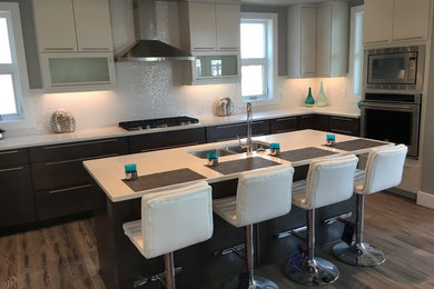Example of a mid-sized trendy medium tone wood floor and brown floor kitchen design in Edmonton with an undermount sink, flat-panel cabinets, white cabinets, white backsplash, stainless steel appliances and an island