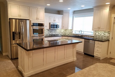 Eat-in kitchen - mid-sized transitional l-shaped porcelain tile and beige floor eat-in kitchen idea in Salt Lake City with raised-panel cabinets, white cabinets, granite countertops, multicolored backsplash, glass tile backsplash, stainless steel appliances, an undermount sink and an island