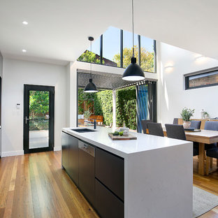 Photo of a contemporary galley open plan kitchen in Sydney with an undermount sink, flat-panel cabinets, black cabinets, marble benchtops, stainless steel appliances, medium hardwood floors, with island, brown floor and white benchtop.