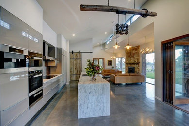 Bild på ett lantligt linjärt kök med öppen planlösning, med en undermonterad diskho, släta luckor, grå skåp, rostfria vitvaror, betonggolv, en köksö och grått golv