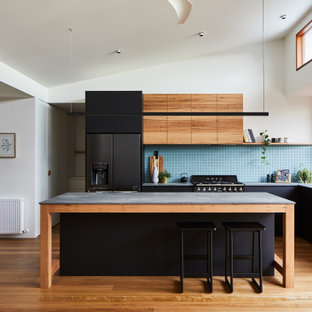 Photo of a contemporary l-shaped kitchen in Melbourne with an undermount sink, flat-panel cabinets, black cabinets, blue splashback, mosaic tile splashback, black appliances, medium hardwood floors, with island, brown floor, grey benchtop and vaulted.