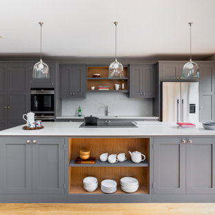 This is an example of a large traditional galley kitchen/diner in London with a submerged sink, shaker cabinets, grey cabinets, quartz worktops, white splashback, engineered quartz splashback, stainless steel appliances, medium hardwood flooring, an island and white worktops.