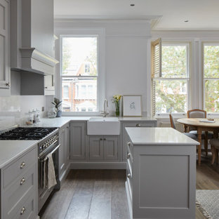 Small traditional l-shaped open plan kitchen in London with a farmhouse sink, grey cabinets, granite benchtops, grey splashback, granite splashback, panelled appliances, dark hardwood floors, with island, brown floor, grey benchtop, coffered and beaded inset cabinets.