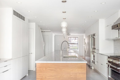 ニューヨークにあるモダンスタイルのおしゃれなアイランドキッチン (フラットパネル扉のキャビネット、濃色木目調キャビネット、大理石カウンター、ライムストーンの床、グレーの床、白いキッチンカウンター) の写真