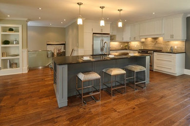 Example of a large transitional l-shaped medium tone wood floor eat-in kitchen design in Burlington with an undermount sink, shaker cabinets, white cabinets, soapstone countertops, beige backsplash, stone tile backsplash, stainless steel appliances and an island