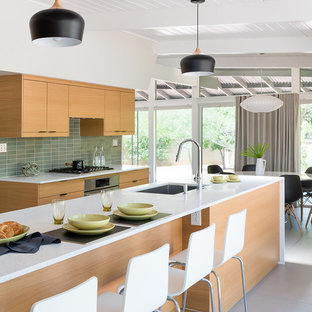This is an example of a mid-sized midcentury galley open plan kitchen in Phoenix with an undermount sink, flat-panel cabinets, medium wood cabinets, quartz benchtops, green splashback, ceramic splashback, stainless steel appliances, porcelain floors, with island and grey floor.
