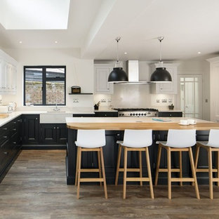 Photo of a traditional kitchen in Other with a belfast sink, recessed-panel cabinets, black cabinets, white splashback, stainless steel appliances, dark hardwood flooring, an island, brown floors and white worktops.