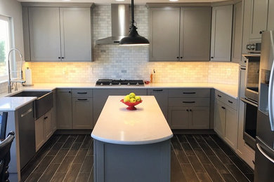Example of a trendy u-shaped kitchen design in Denver with a farmhouse sink, shaker cabinets, gray cabinets, quartz countertops, gray backsplash, stainless steel appliances and an island