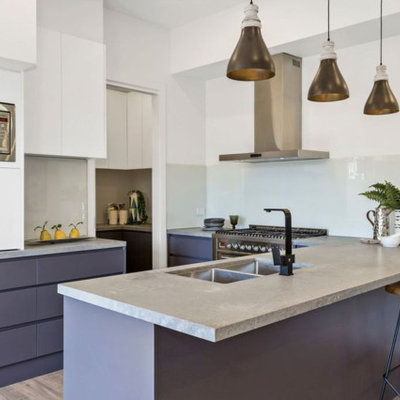 Inspiration for a contemporary light wood floor kitchen remodel in Melbourne with a double-bowl sink, flat-panel cabinets, white cabinets, concrete countertops, white backsplash, glass sheet backsplash, stainless steel appliances, a peninsula and gray countertops