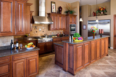Eat-in kitchen - mid-sized transitional galley porcelain tile eat-in kitchen idea in Phoenix with a double-bowl sink, raised-panel cabinets, medium tone wood cabinets, solid surface countertops, beige backsplash, stone tile backsplash, stainless steel appliances and an island