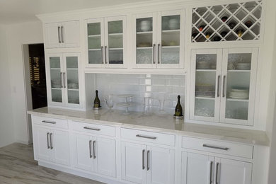 Example of a mid-sized transitional u-shaped porcelain tile and gray floor eat-in kitchen design in Los Angeles with a farmhouse sink, recessed-panel cabinets, white cabinets, solid surface countertops, white backsplash, subway tile backsplash, stainless steel appliances, an island and white countertops