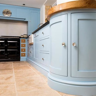 Photo of a small traditional u-shaped separate kitchen in Oxfordshire with a single-bowl sink, blue cabinets, granite benchtops, black splashback, black appliances, limestone floors and no island.