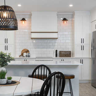 Beach style l-shaped eat-in kitchen in Sunshine Coast with a drop-in sink, shaker cabinets, white cabinets, white splashback, subway tile splashback, stainless steel appliances, a peninsula, grey floor and white benchtop.