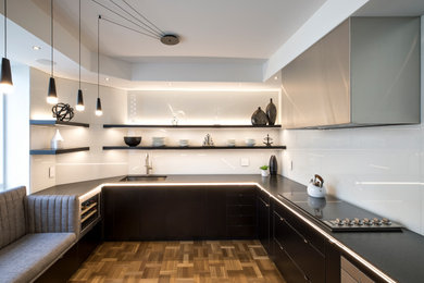 Example of a small trendy u-shaped light wood floor and brown floor enclosed kitchen design in Toronto with an undermount sink, flat-panel cabinets, black cabinets, granite countertops, white backsplash, glass sheet backsplash, stainless steel appliances, no island and black countertops