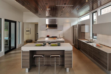 This is an example of a large contemporary l-shaped kitchen/diner in Houston with a submerged sink, flat-panel cabinets, grey cabinets, stainless steel appliances, quartz worktops, white splashback, glass sheet splashback, porcelain flooring, multiple islands and brown floors.