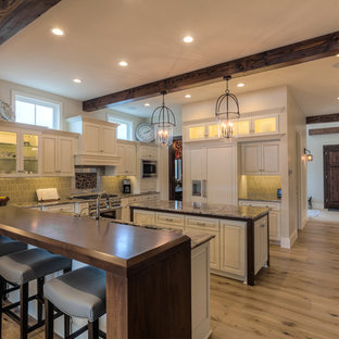 Large country u-shaped separate kitchen in Seattle with multiple islands, an undermount sink, raised-panel cabinets, white cabinets, granite benchtops, grey splashback, stainless steel appliances and light hardwood floors.