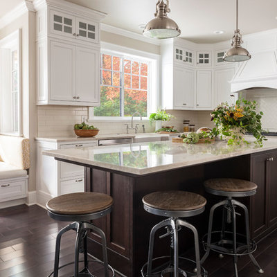 Mid-sized country l-shaped dark wood floor and brown floor eat-in kitchen photo in Seattle with a farmhouse sink, shaker cabinets, white cabinets, white backsplash, subway tile backsplash, an island and stainless steel appliances