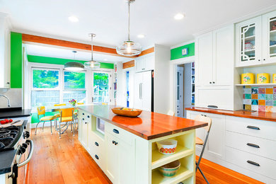 Inspiration for a mid-sized eclectic galley light wood floor eat-in kitchen remodel in Boston with a farmhouse sink, shaker cabinets, yellow cabinets, wood countertops, multicolored backsplash, ceramic backsplash, paneled appliances and an island