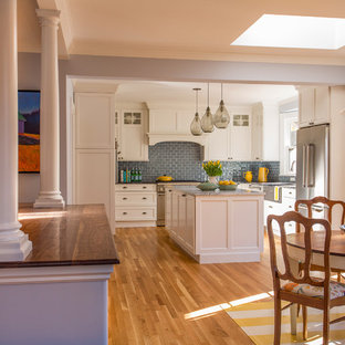 Design ideas for a large victorian l-shaped eat-in kitchen in Boston with a farmhouse sink, shaker cabinets, white cabinets, marble benchtops, glass tile splashback, stainless steel appliances, medium hardwood floors, blue splashback and multiple islands.