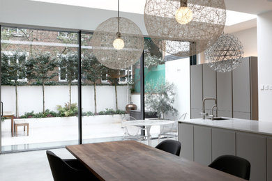Inspiration for a large contemporary kitchen/diner in London with a built-in sink, flat-panel cabinets, grey cabinets, white splashback, black appliances, concrete flooring, an island, grey floors and white worktops.